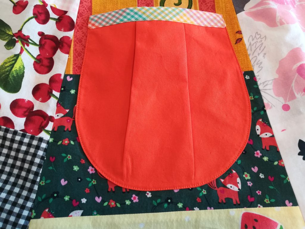 Op de bevrijdingsrok zit een opgestikte zak van oranje stof, aan de bovenkant afgewerkt met regenboogkleurig boerenbont biaisband.