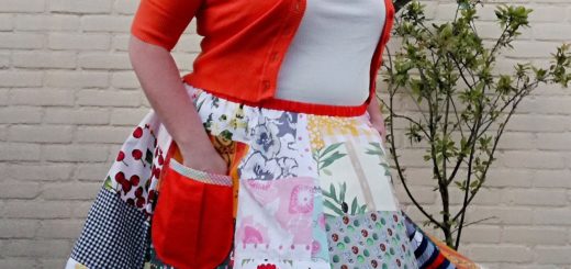 Suzanne poseert voor een muur met een schildering van een boom, in een oranje vestje en een rok gemaakt van veel kleurrijke lapjes